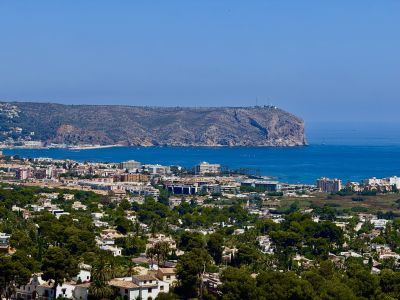 Vue panoramique étendue présentant le paysage résidentiel de Jávea, la mer Méditerranée d'un bleu profond avec des bateaux et le cap rocheux proéminent avec son phare.