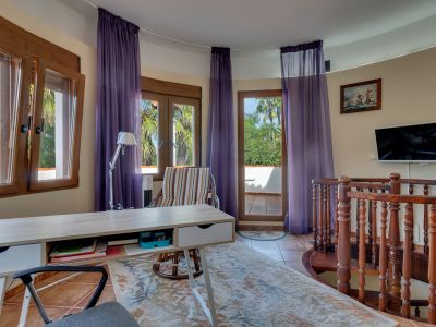 Bureau lumineux avec un bureau en bois clair, sol carrelé et mur incurvé avec grandes fenêtres et accès à une terrasse verdoyante. Un escalier en colimaçon en bois est présent.