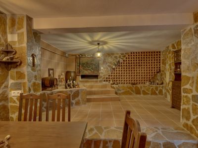 Cave rustique aux murs en pierre naturelle et carrelage en terre cuite. Elle présente un casier à vin intégré et une niche étagée, éclairée par un luminaire central créant un motif unique au plafond.