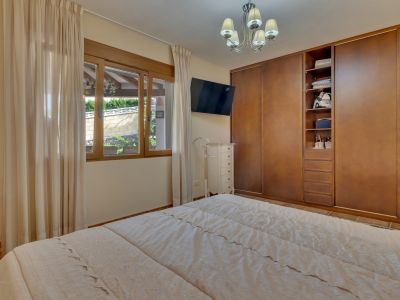 Chambre avec lit double, placards intégrés en bois et fenêtre donnant sur un mur paysager. Comprend une télévision murale et une commode blanche.
