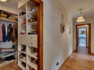 Couloir avec armoire ouverte intégrée à étagères blanches et tiroirs, carrelage en terre cuite et encadrements de portes en bois.