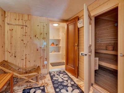 Espace de détente avec murs en bois clair et carrelage au sol, offrant un accès direct à un sauna en pin. Comprend un fauteuil en bois et une entrée vers un espace de rangement.