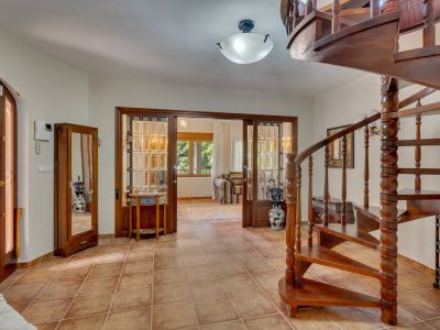 Hall d'entrée avec escalier en colimaçon en bois foncé et carrelage en terre cuite. Des portes coulissantes vitrées mènent à une pièce adjacente lumineuse.