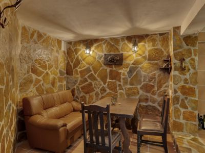 Intérieur avec murs en pierre irrégulière et sol carrelé. Comprend un canapé en cuir, une table en bois rustique et un éclairage mural chaleureux de lanternes.