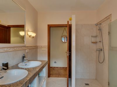 Salle de bain principale avec double vasque sur comptoir en granit, grand miroir encadré et douche à l'italienne avec paroi vitrée, soulignée par des carreaux aux tons chauds.