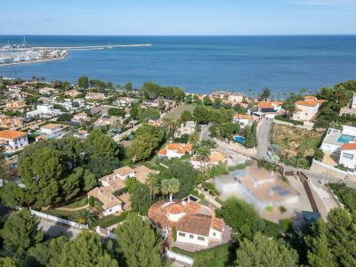 Vue aérienne du quartier résidentiel de Dénia, présentant des villas, une végétation luxuriante et le port de plaisance en bord de mer.
