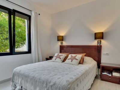 Chambre lumineuse avec lit double, tête de lit en bois foncé et coussins à étoiles de mer. La fenêtre ouverte à cadres noirs offre une vue sur la verdure extérieure.