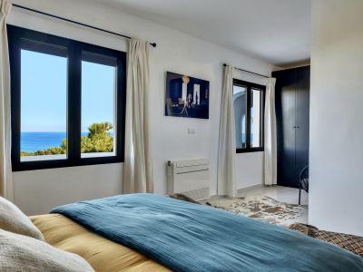Chambre lumineuse offrant une vue directe sur la mer Méditerranée par des fenêtres à cadre sombre. Elle dispose d'une armoire intégrée et de la climatisation.