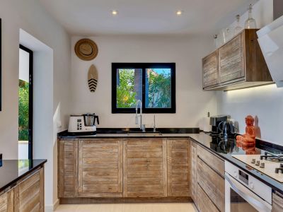Cuisine équipée avec des armoires en bois rustique, des plans de travail noirs et une fenêtre donnant sur le jardin. Appareils modernes et double évier.