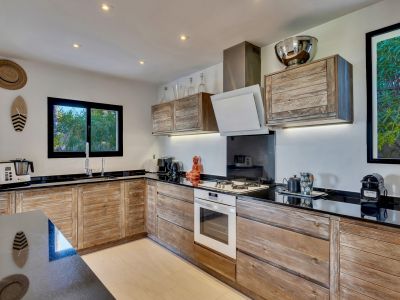 Cuisine équipée avec des armoires en bois rustique et des plans de travail noirs. Une fenêtre au-dessus de l'évier offre une vue sur la verdure extérieure.