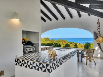 Cuisine extérieure sous une terrasse couverte avec comptoir carrelé géométrique noir et blanc, barbecue intégré et vue panoramique sur la mer Méditerranée par une arche.
