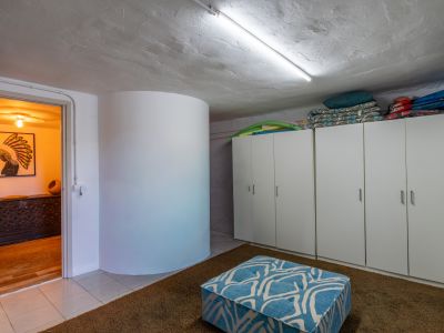 Espace fonctionnel doté d'armoires de rangement blanches, d'un plafond texturé avec éclairage fluorescent et d'un tapis shaggy marron. Un pouf bleu à motifs et une ouverture sur une pièce adjacente chaleureuse.