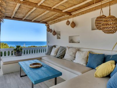 Terrasse couverte avec banquette intégrée, coussins colorés et table basse en bois bleu. Le plafond en canisse naturelle offre une vue imprenable sur la mer Méditerranée.