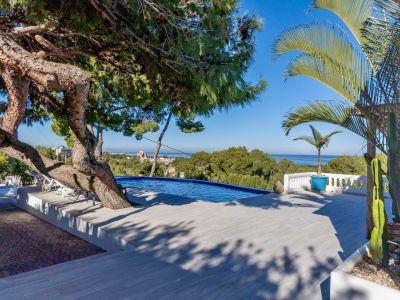 Terrasse de piscine à débordement avec carrelage clair, bordée d'un pin mature et d'une balustrade blanche. Vues panoramiques sur la mer et transats.