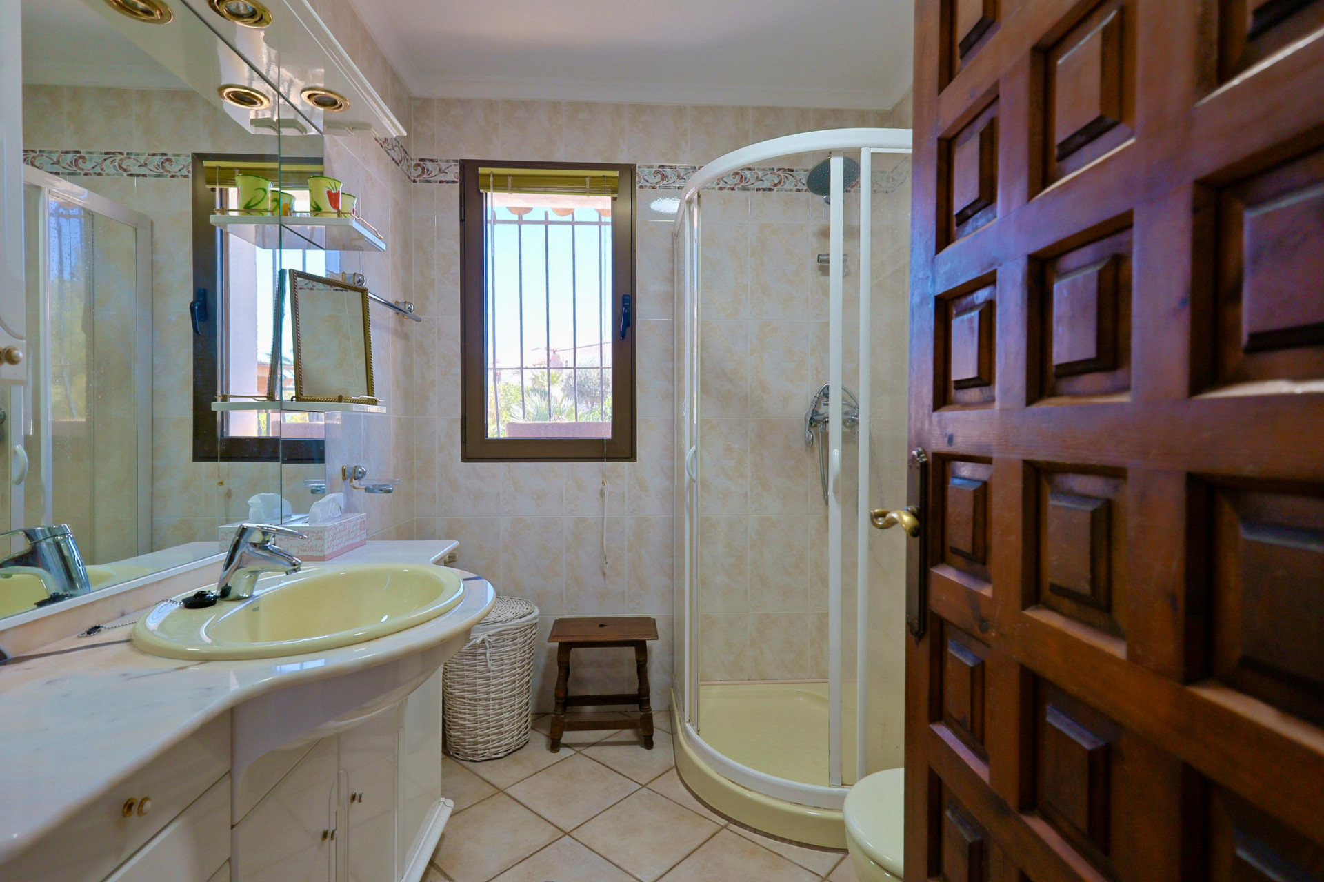 Détail de la salle de bain avec lavabo jaune, douche d'angle et porte en bois sculpté.