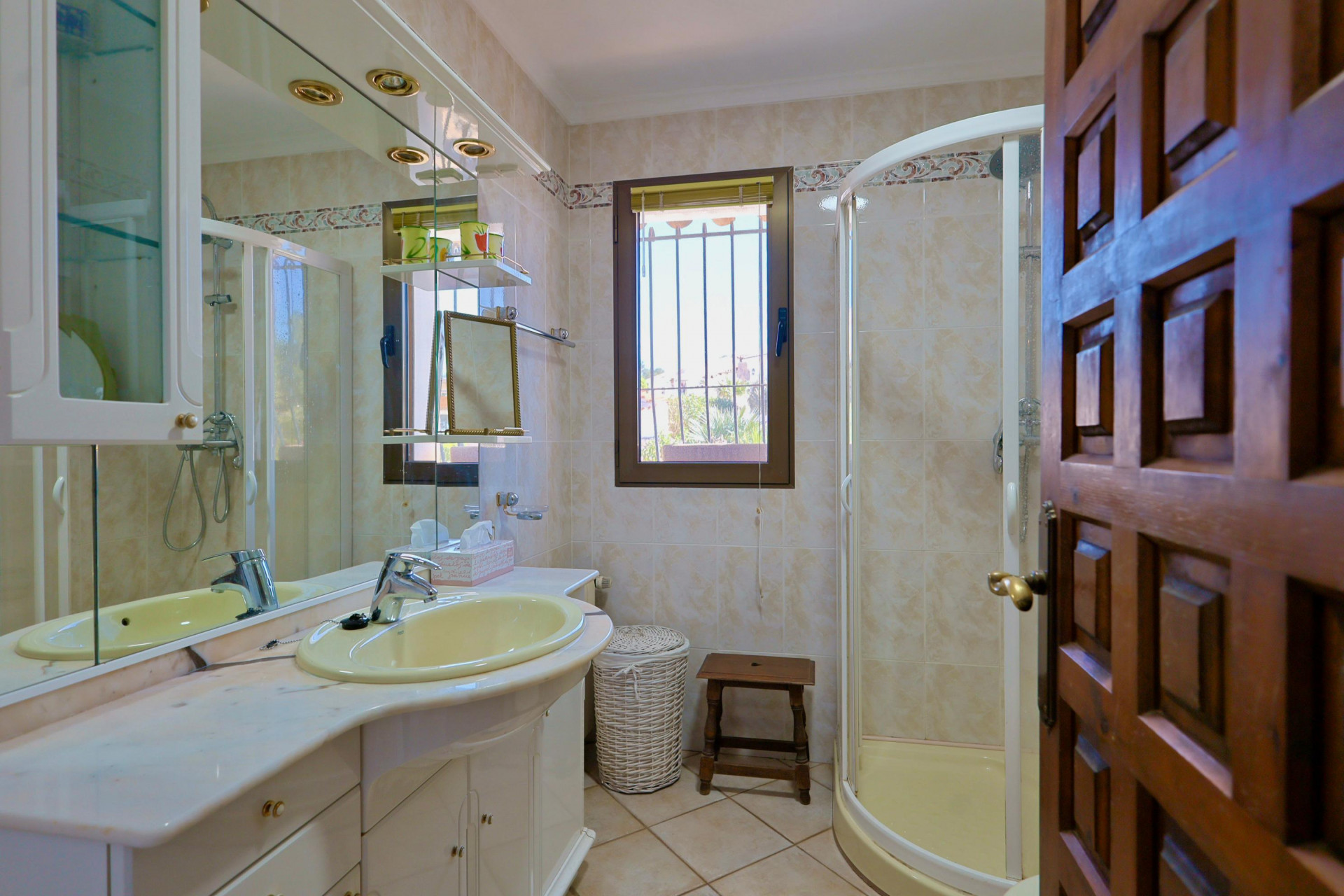 Détail de salle de bain avec lavabo jaune, douche d'angle et porte en bois sculpté.