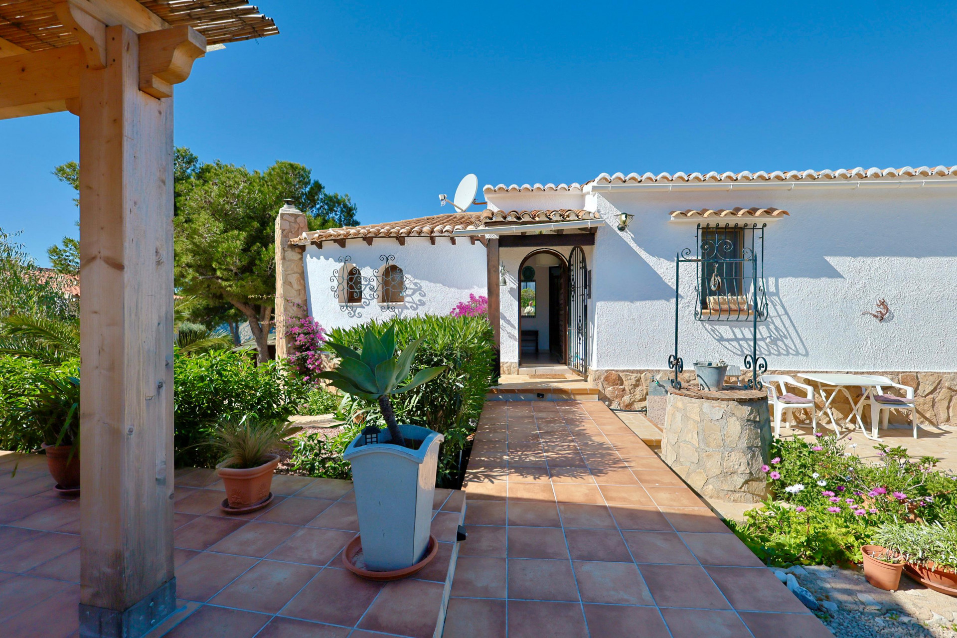 Entrée de la villa avec puits décoratif, jardin et terrasse carrelée.