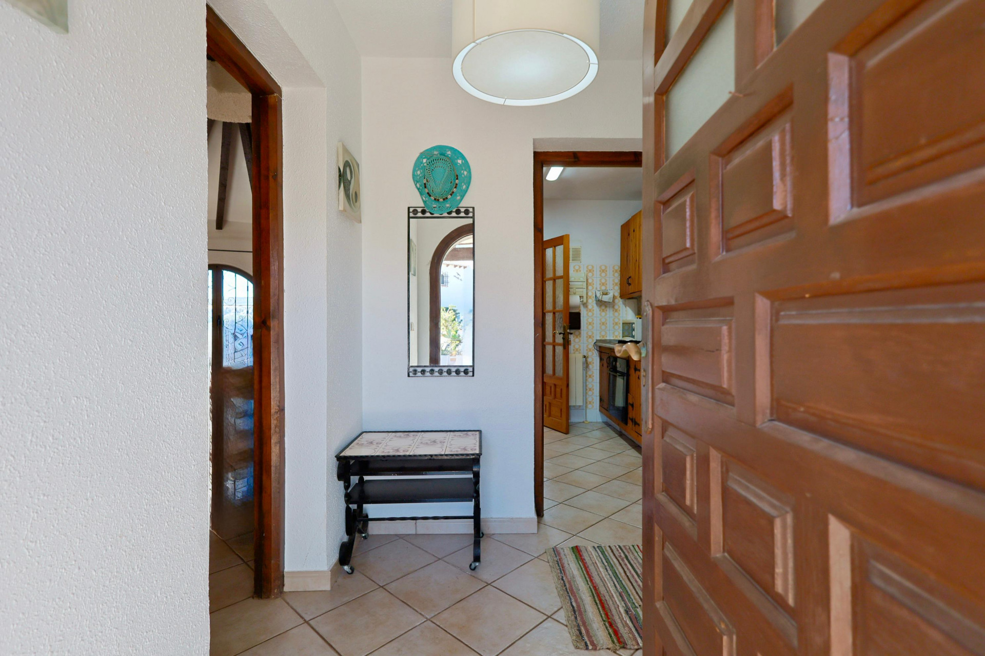 Entrée lumineuse avec miroir décoratif et porte en bois massif entrouverte sur la cuisine.