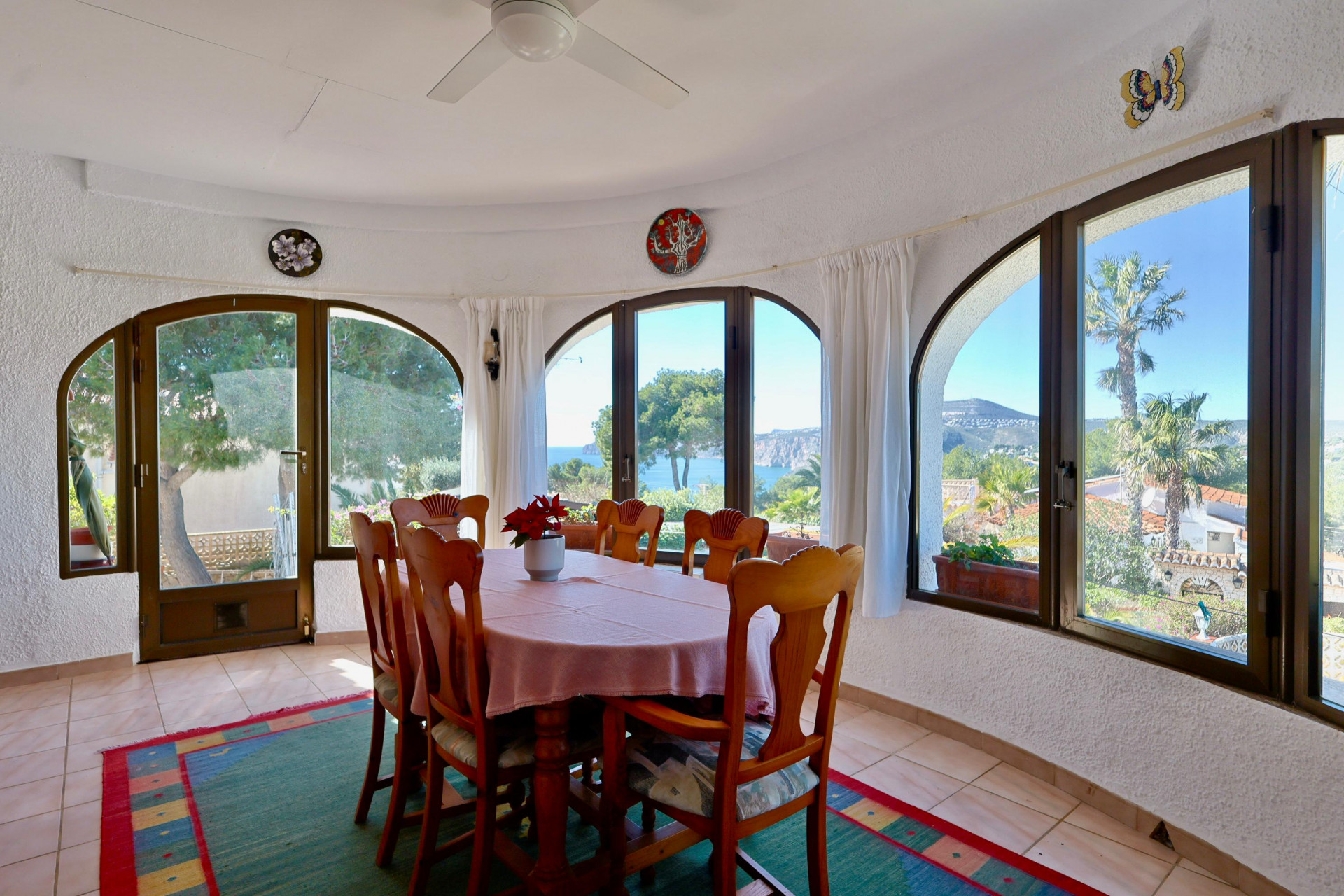 Salle à manger lumineuse avec vue sur la mer, entourée de fenêtres cintrées et d'un décor rustique.