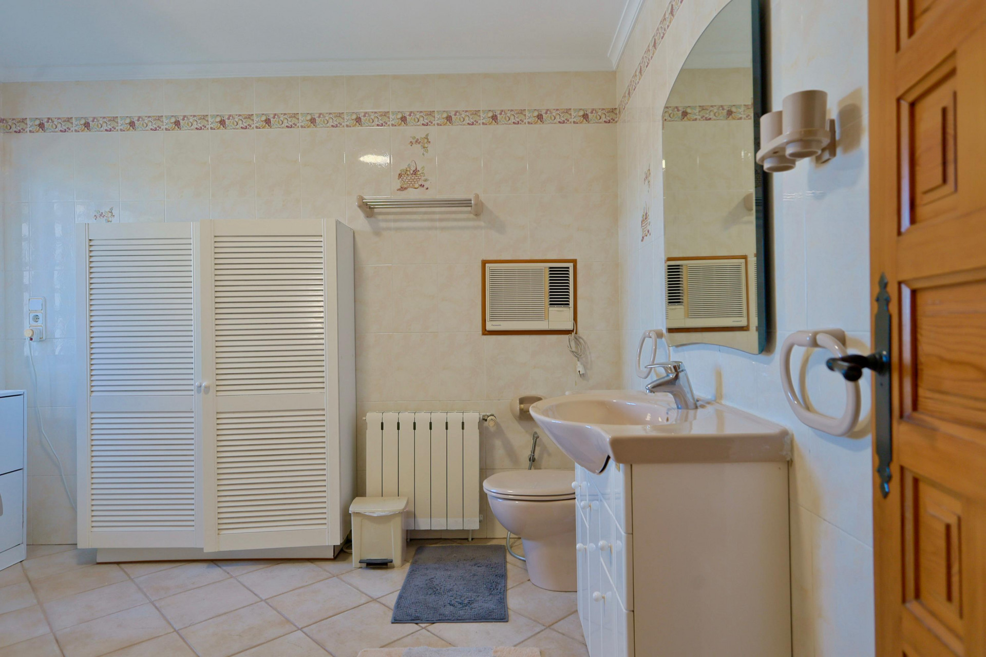 Salle de bain carrelée avec armoire à persiennes blanche et lavabo à comptoir beige.