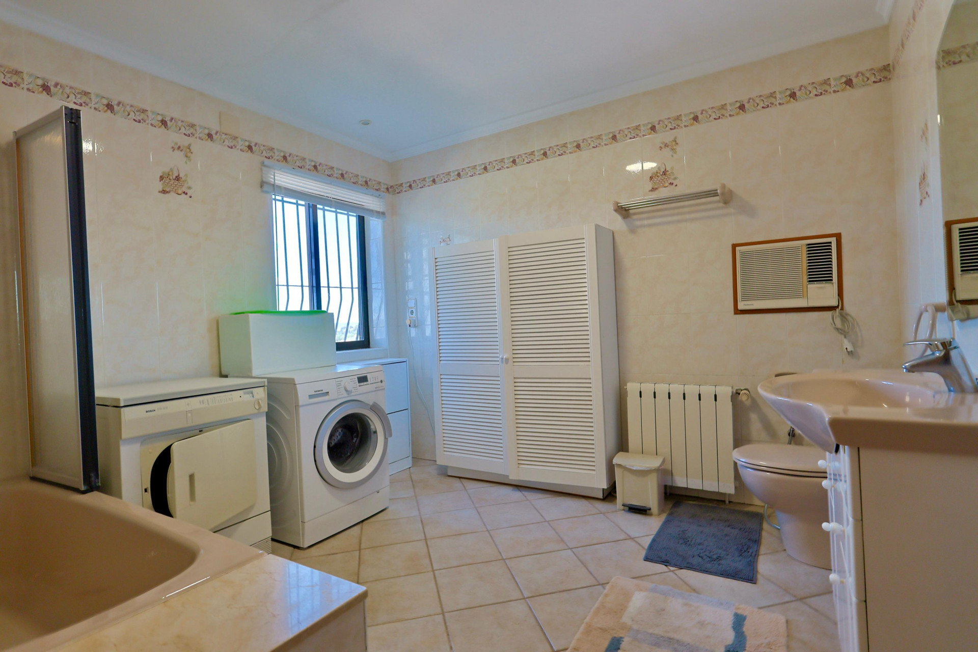 Salle de bain fonctionnelle avec lave-linge, sèche-linge et grande armoire à persiennes blanches.