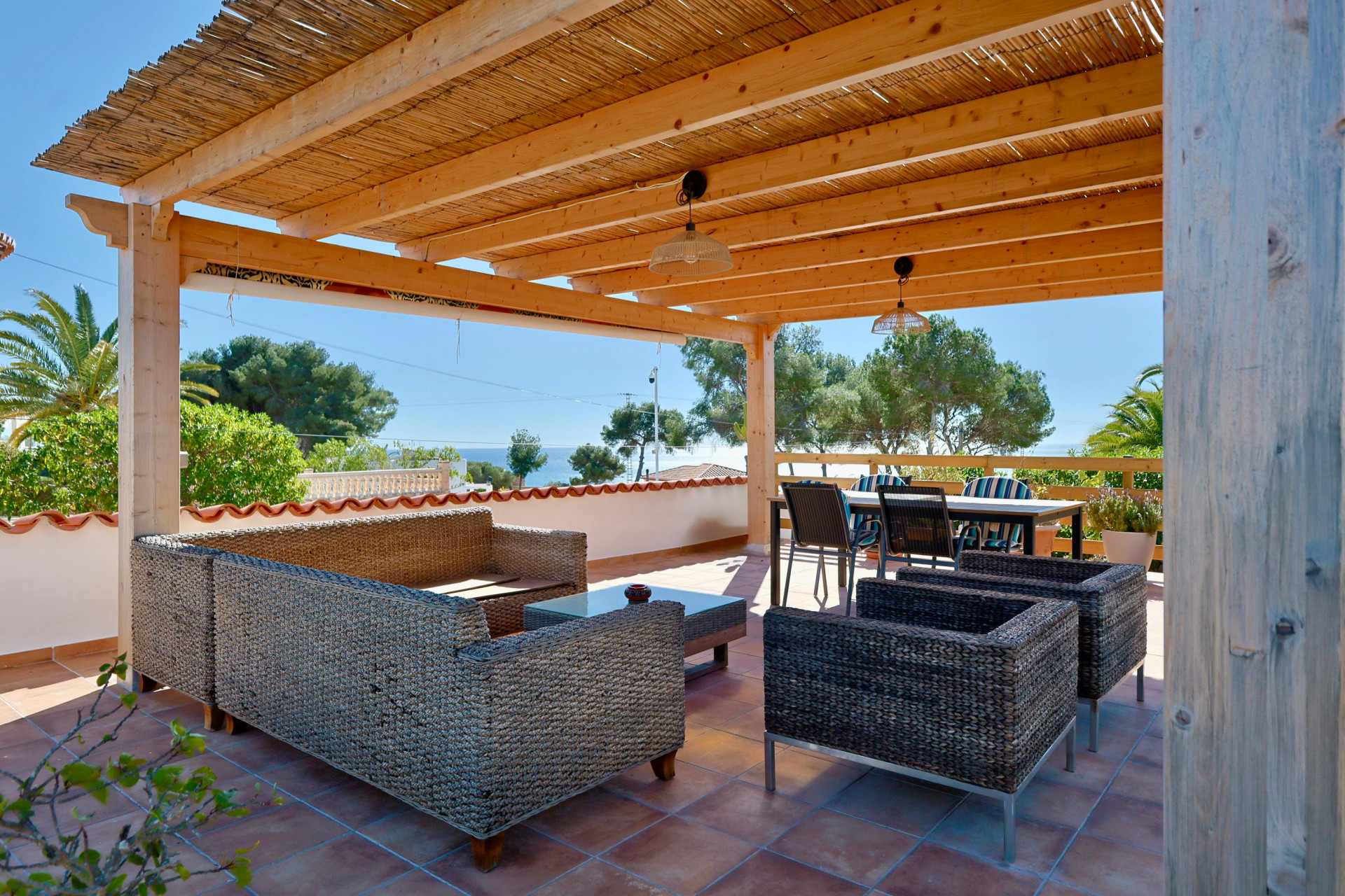 Terrasse couverte avec mobilier en rotin et vue sur la mer.
