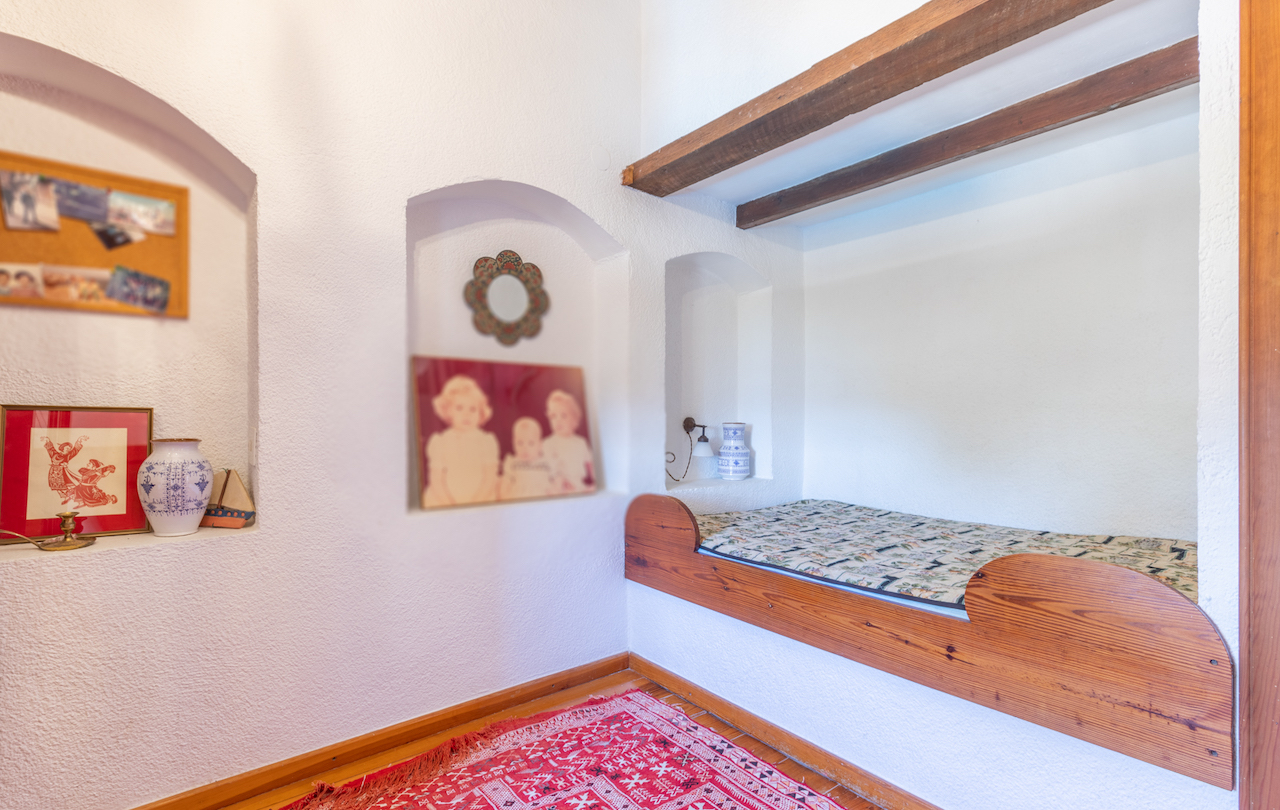 Chambre rustique avec lit encastré en bois, poutres apparentes et niches murales décoratives intégrées dans des murs blancs de style traditionnel.