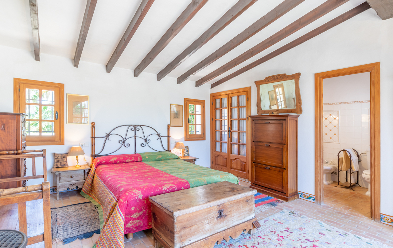 Chambre rustique avec poutres en bois apparentes, sol en terre cuite et mobilier traditionnel. Elle dispose d'un accès direct à une salle de bain attenante.