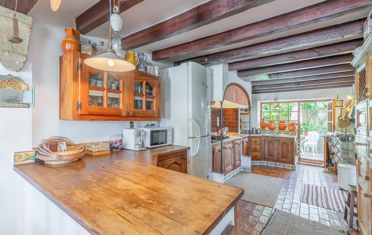 Cuisine de style traditionnel avec poutres en bois apparentes, plans de travail en bois massif et accès direct à un patio verdoyant.