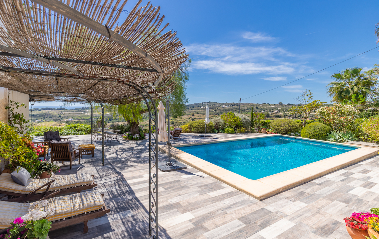 Espace piscine avec terrasse en dalles antidérapantes et pergola rustique en fer forgé et canisse. Vue dégagée sur la vallée et les jardins méditerranéens environnants.