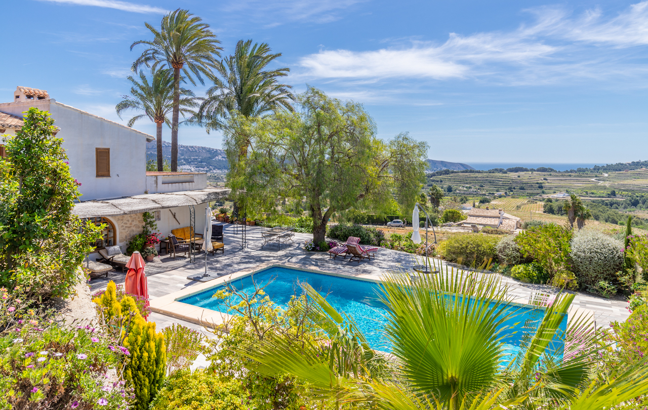 Espace piscine avec terrasse en pierre et jardin méditerranéen, offrant une vue dégagée sur les vignobles et la mer Méditerranée à l'horizon.