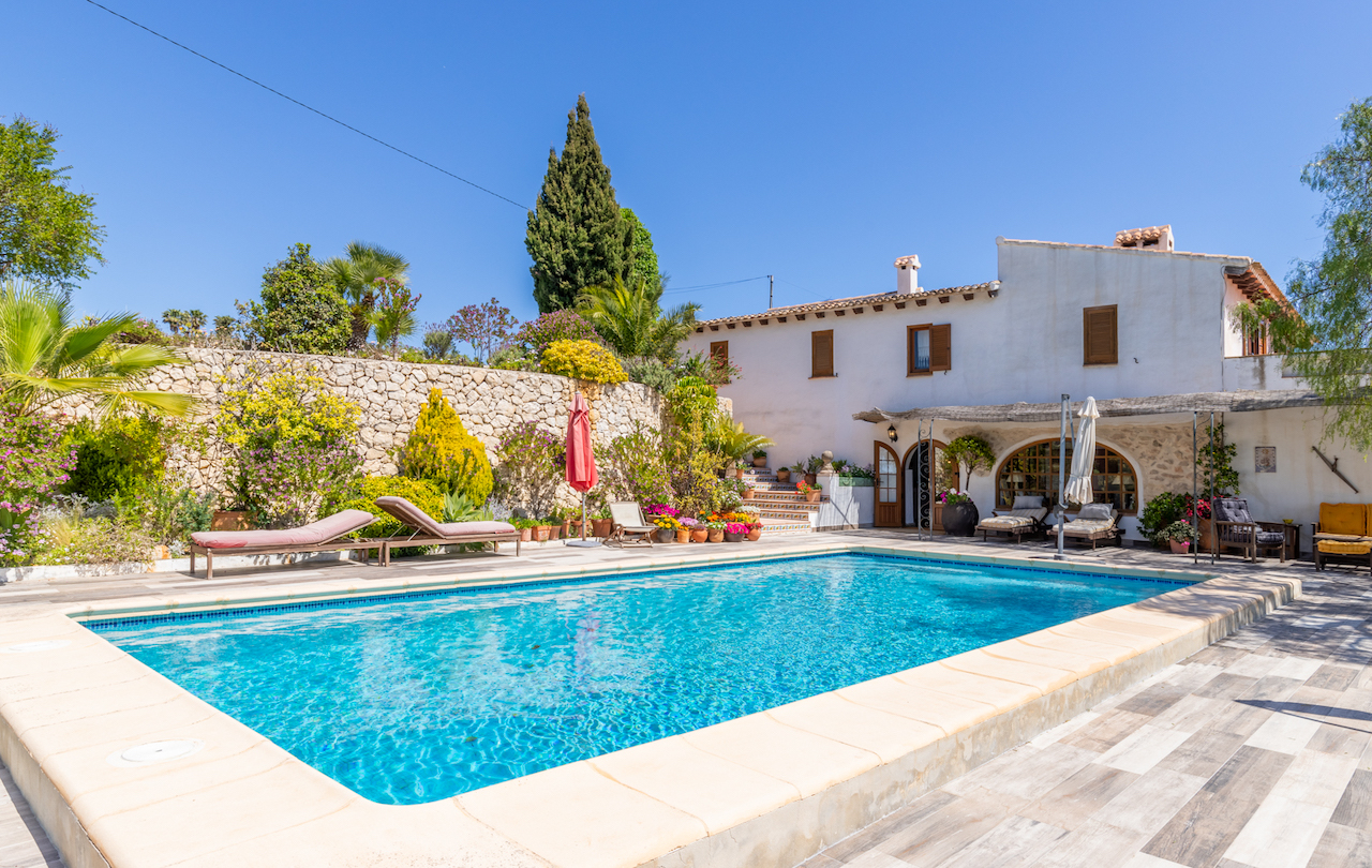 Piscine rectangulaire entourée d'une terrasse antidérapante, de murs en pierre sèche et d'un jardin méditerranéen luxuriant bordant la maison de style traditionnel.