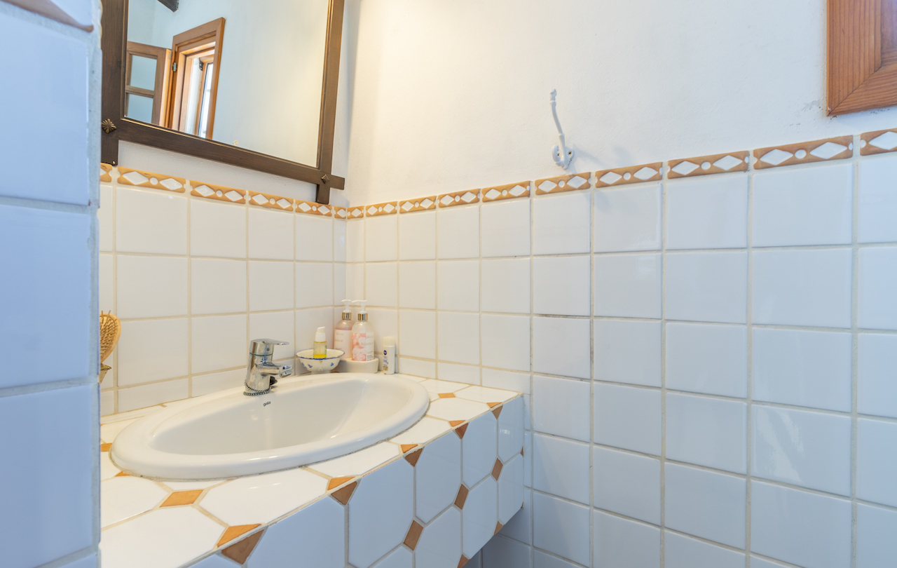 Salle de bain de style traditionnel avec carrelage blanc et frise décorative. Lavabo encastré sur un plan de travail carrelé aux motifs géométriques et miroir à cadre en bois.
