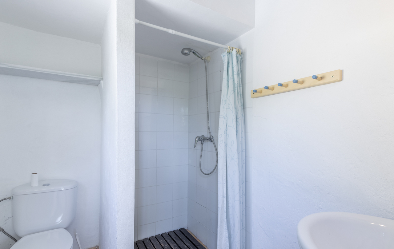 Salle de bain fonctionnelle avec douche à l'italienne carrelée, caillebotis en bois sombre, rideau à motifs et patère en bois aux accents bleus.