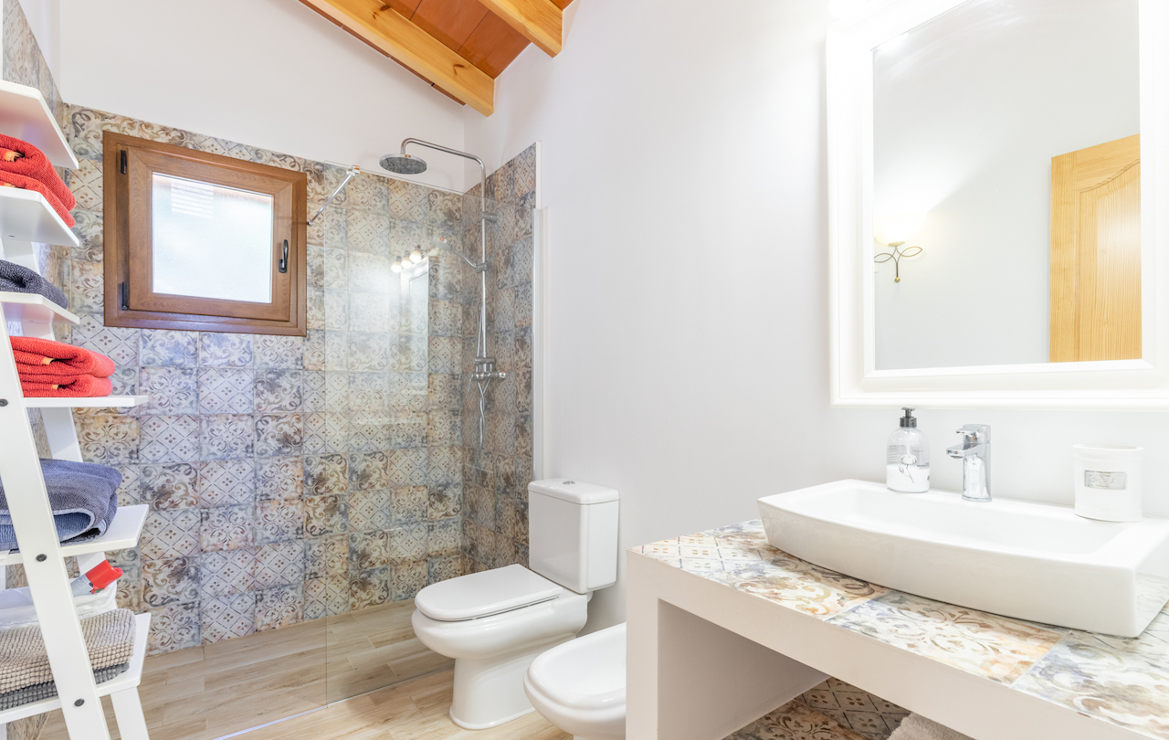 Salle de bains avec plafond en poutres de bois, douche à l'italienne aux carreaux de ciment et plan de vasque assorti avec sanitaires blancs modernes.