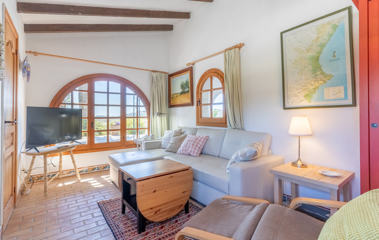 Salon rustique avec poutres en bois apparentes, sol en terre cuite et fenêtres cintrées en bois offrant une lumière naturelle et des vues sur le jardin.