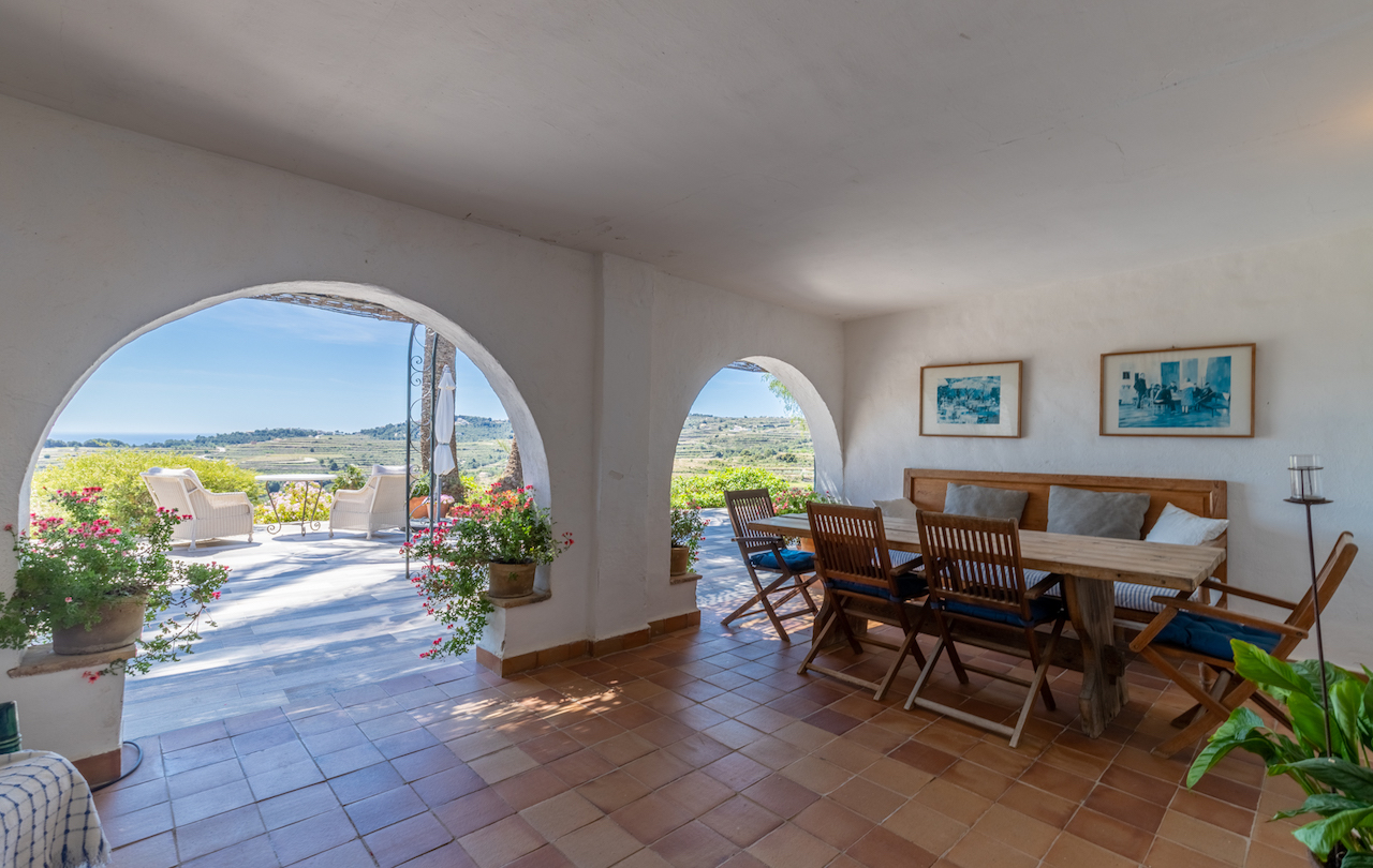 Terrasse couverte avec arches traditionnelles, sol en terre cuite et coin repas rustique. Elle offre une vue dégagée sur les vignobles et la mer Méditerranée.