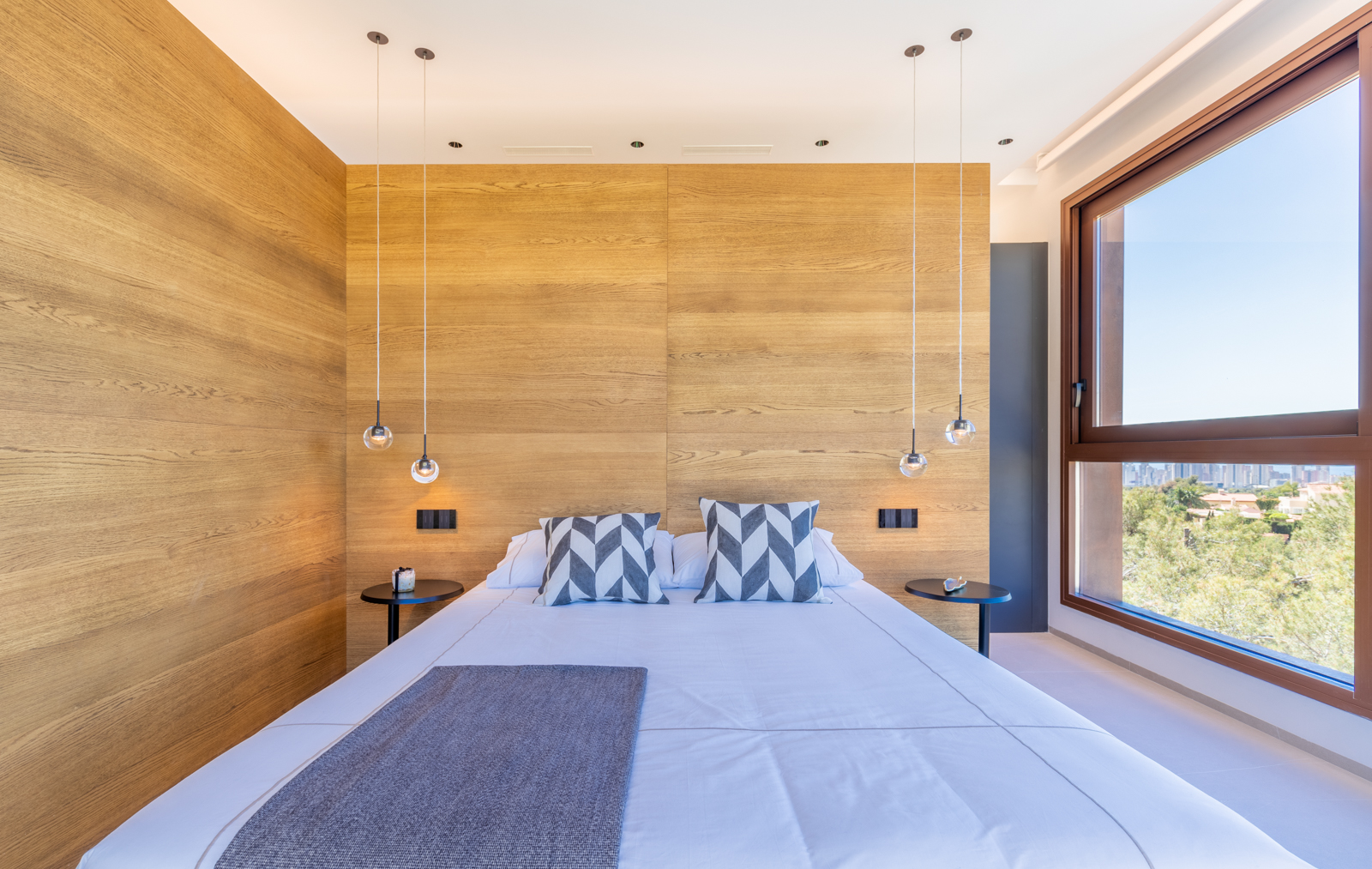 Chambre avec mur en bois clair, suspensions sphériques et vue sur l'extérieur.