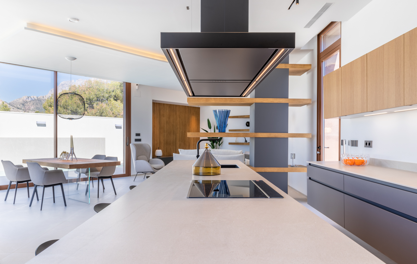 Détail de la cuisine moderne avec îlot central, hotte noire et étagères ouvertes en bois.
