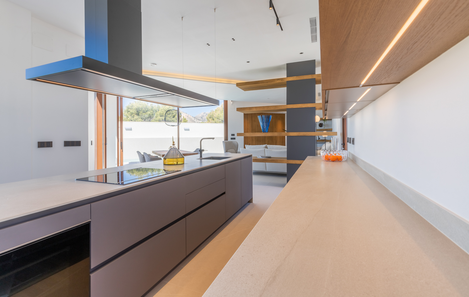 Détail de la cuisine moderne avec îlot gris, comptoir beige et étagères en bois éclairées.