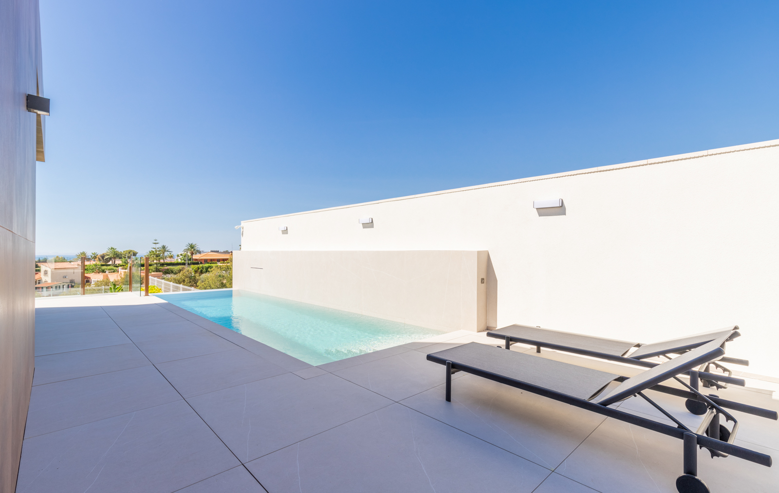 Détail de la piscine à débordement avec vue et chaises longues sur carrelage gris.