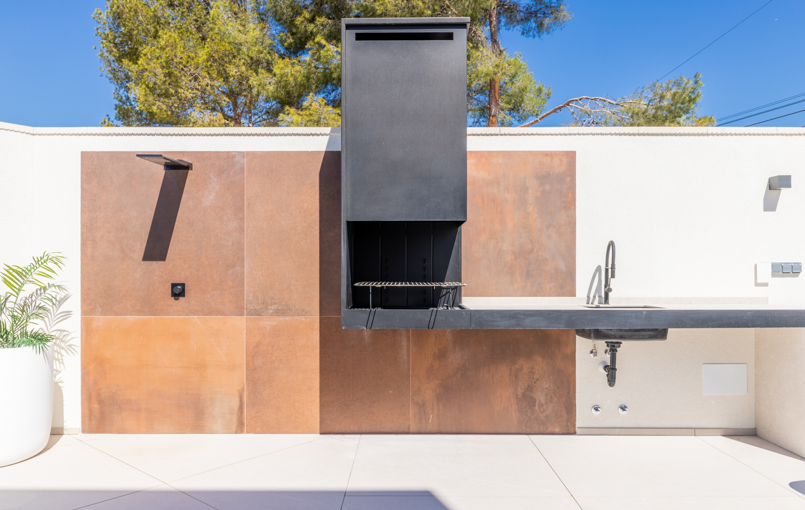 Détail de l'espace barbecue extérieur avec revêtement en carreaux couleur rouille et évier.