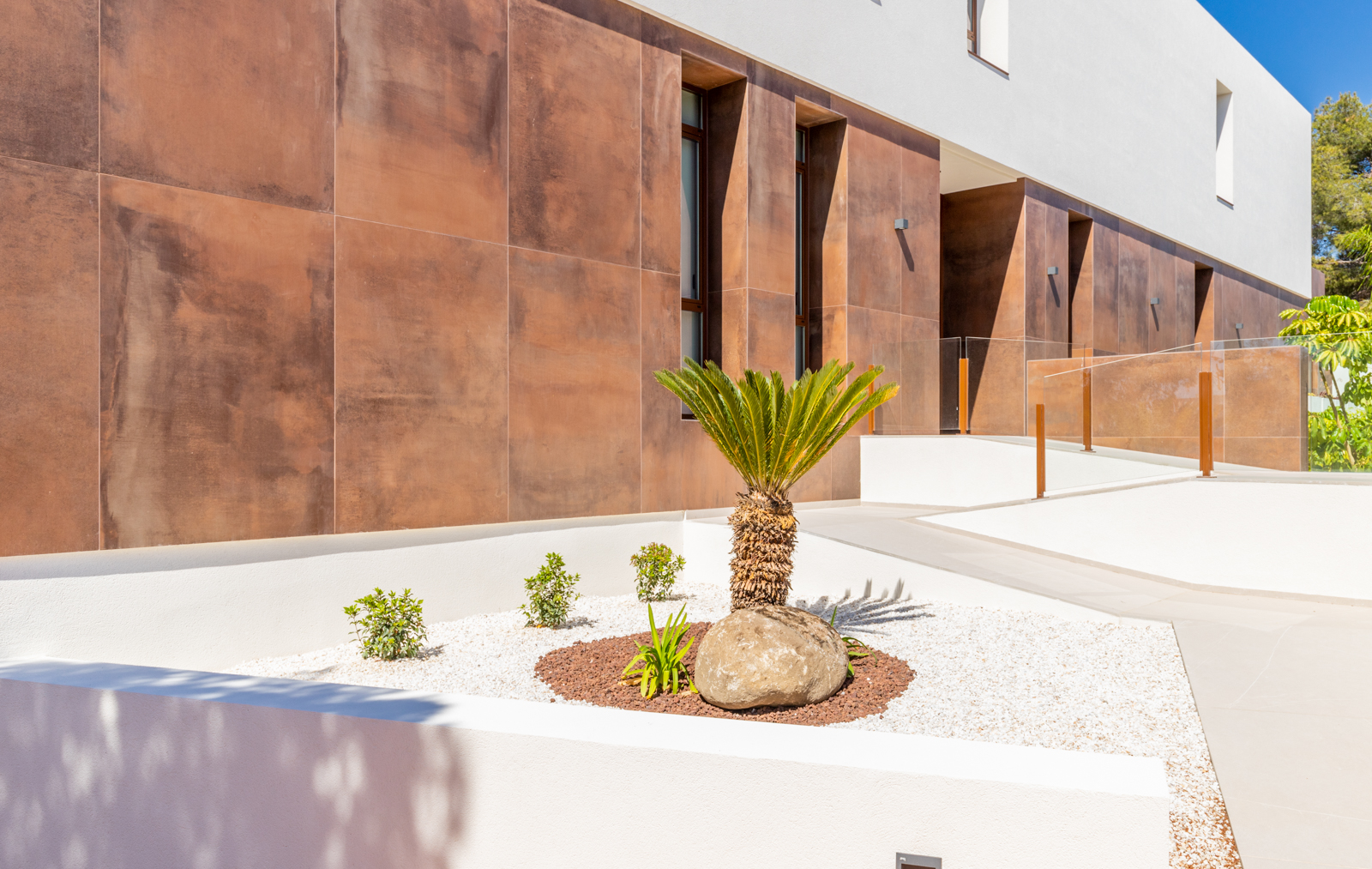 Détail du jardin avant avec mur en panneaux couleur rouille et chemin d'accès.