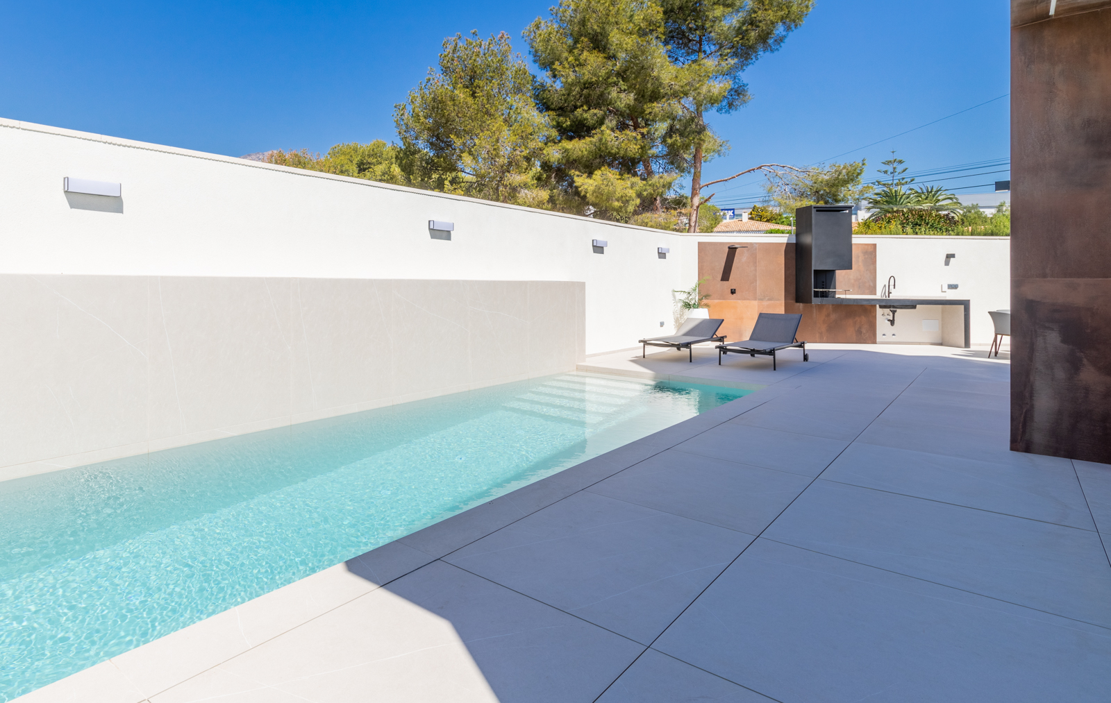 Piscine moderne avec mur carrelé blanc et espace barbecue avec comptoir en béton.
