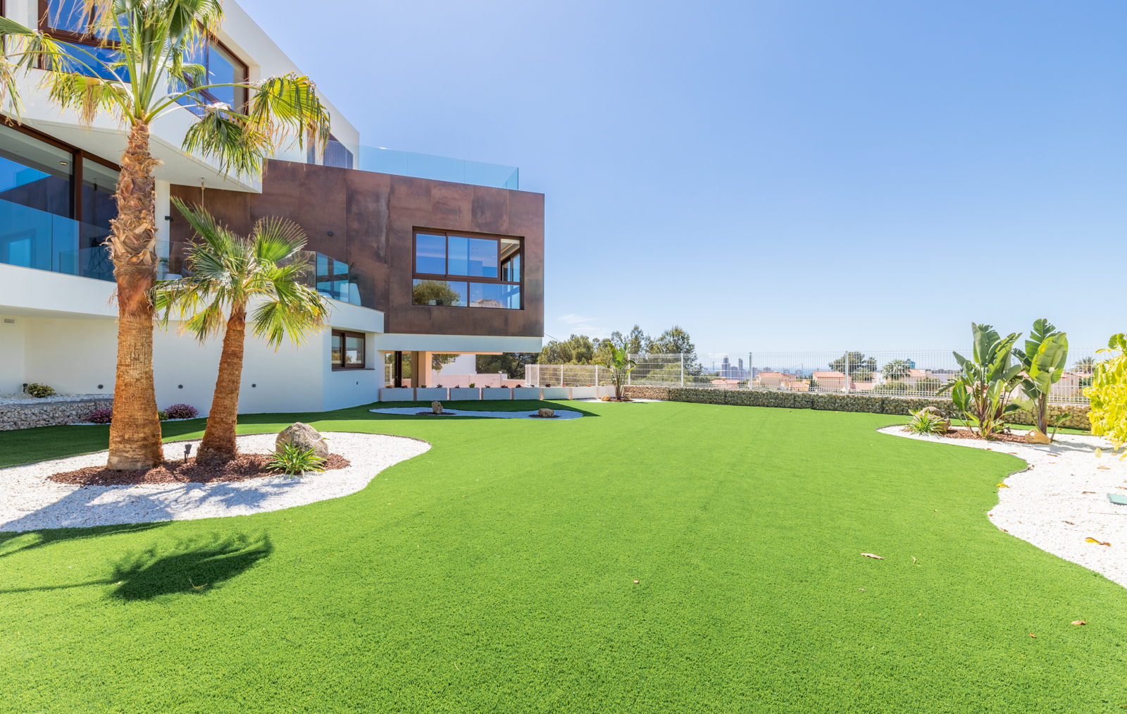 Vue du jardin avec gazon synthétique, palmiers et façade moderne à La Nucía.