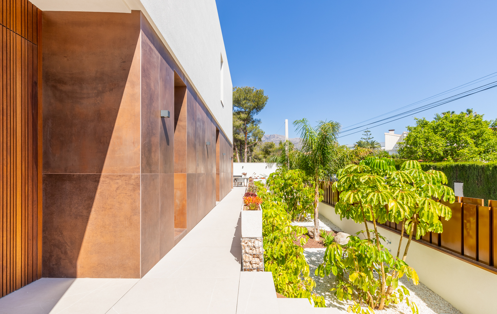 Vue extérieure de la villa avec jardin méditerranéen et mur revêtu de tons terre.