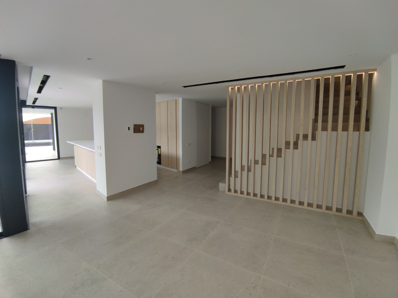 Espace ouvert avec sol en grès cérame, souligné par un escalier design aux lattes de bois verticales et un éclairage LED indirect chaleureux.