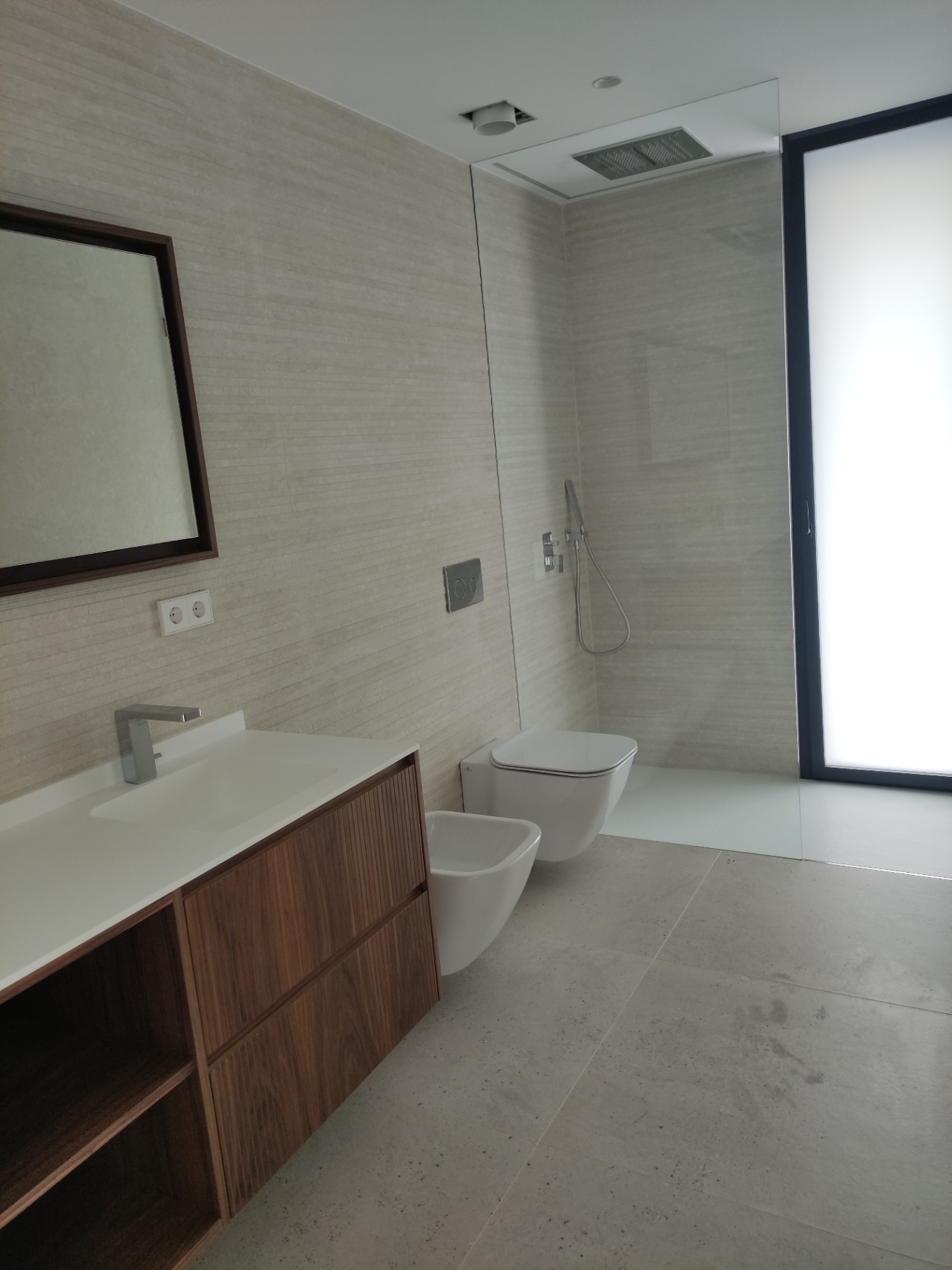 Salle de bains moderne avec meuble sous-vasque en bois, sanitaires suspendus et douche à l'italienne équipée d'un pommeau de plafond et d'une paroi en verre.