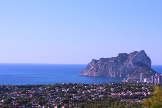 Vue panoramique sur le Peñón de Ifach et la mer Méditerranée, révélant le littoral de Calpe et une végétation dense sous un ciel dégagé.