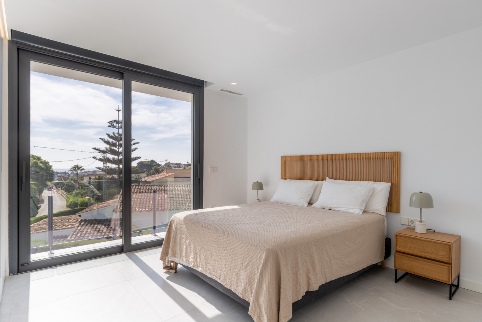 Chambre lumineuse avec lit double, tête de lit en bois et vue sur l'extérieur.